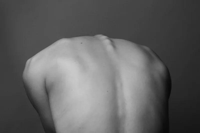 Gri arka planda bir kişinin çıplak sırtının omurga hattını gösteren siyah beyaz fotoğrafı