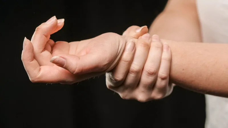 Bir elinin diğer bileğini kavradığı, el bileğinde rahatsızlık hisseden kadın