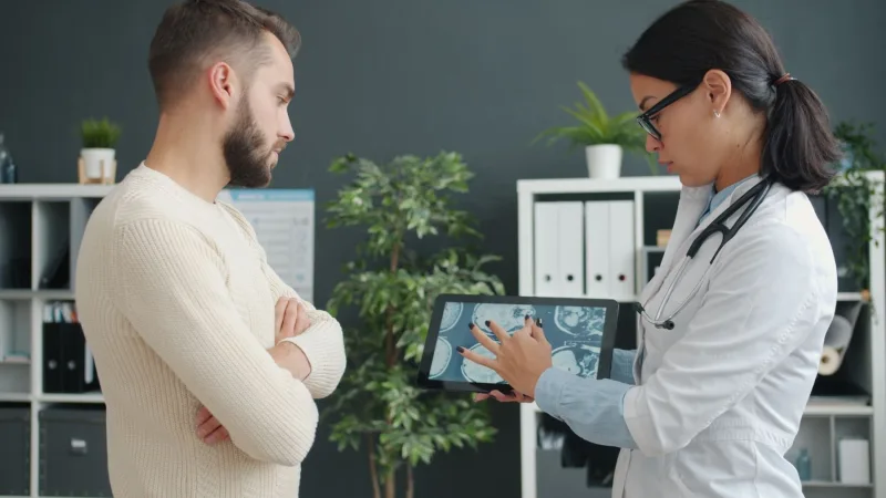Beyaz önlüklü doktorun tablette beyin görüntülerini karşısındaki kişiye gösterdiği an