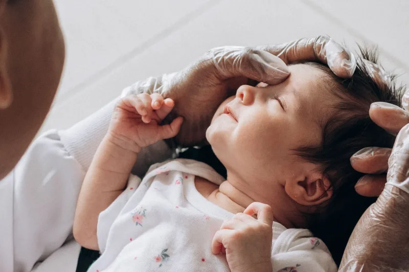 Eldivenli ellerle başı muayene edilen, gözleri kapalı uyuyan yenidoğan bebek
