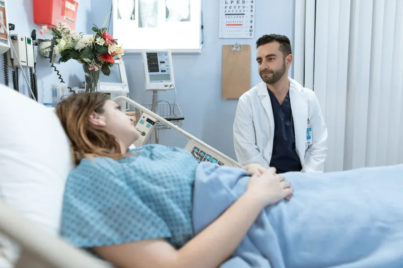 Hastane yatağında yatan hastayla yatağın yanında oturup konuşan beyaz önlüklü doktor